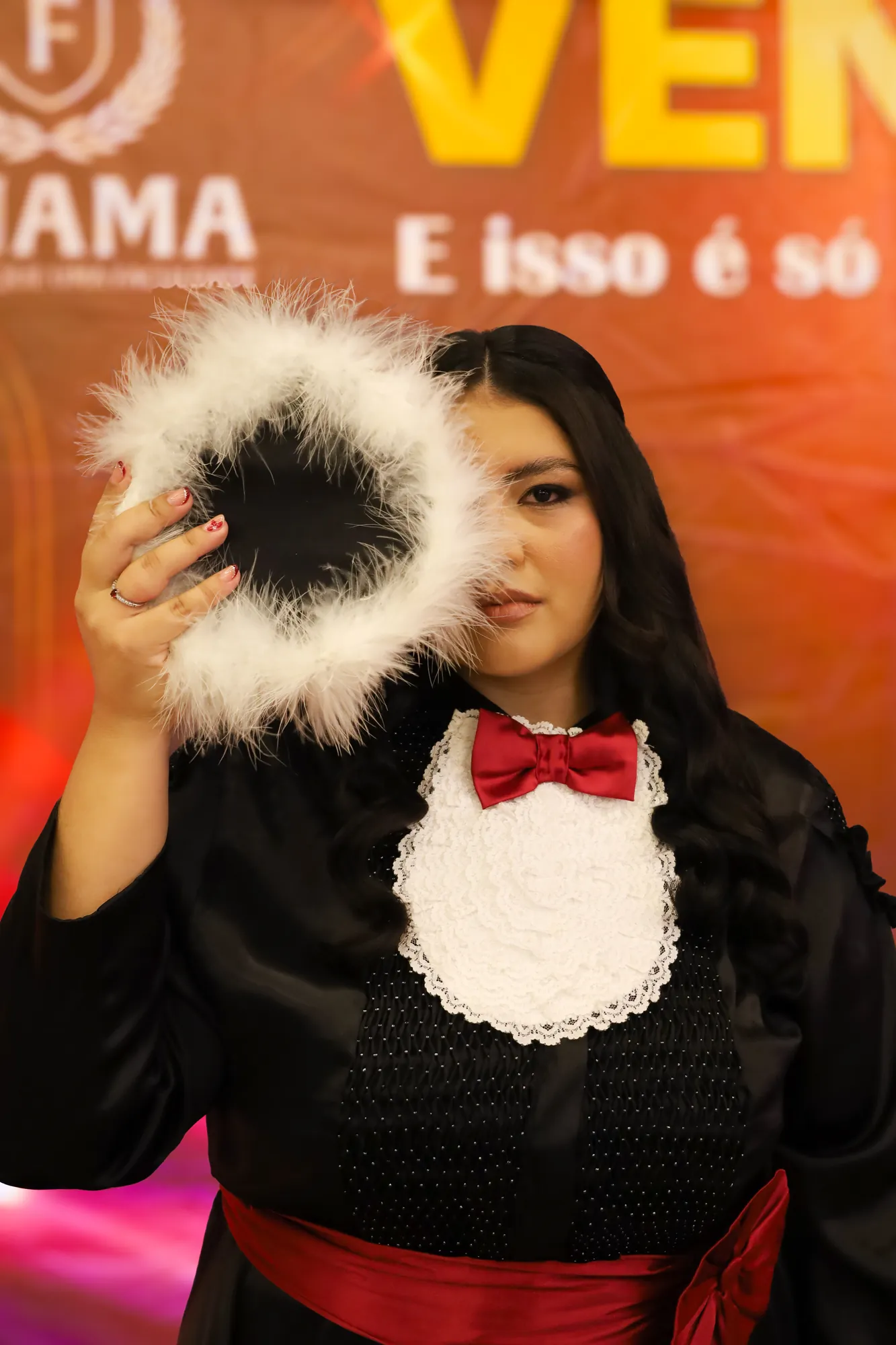 Formanda sorrindo atrás de um capelo de pelúcia branca, de gravata borboleta vermelha