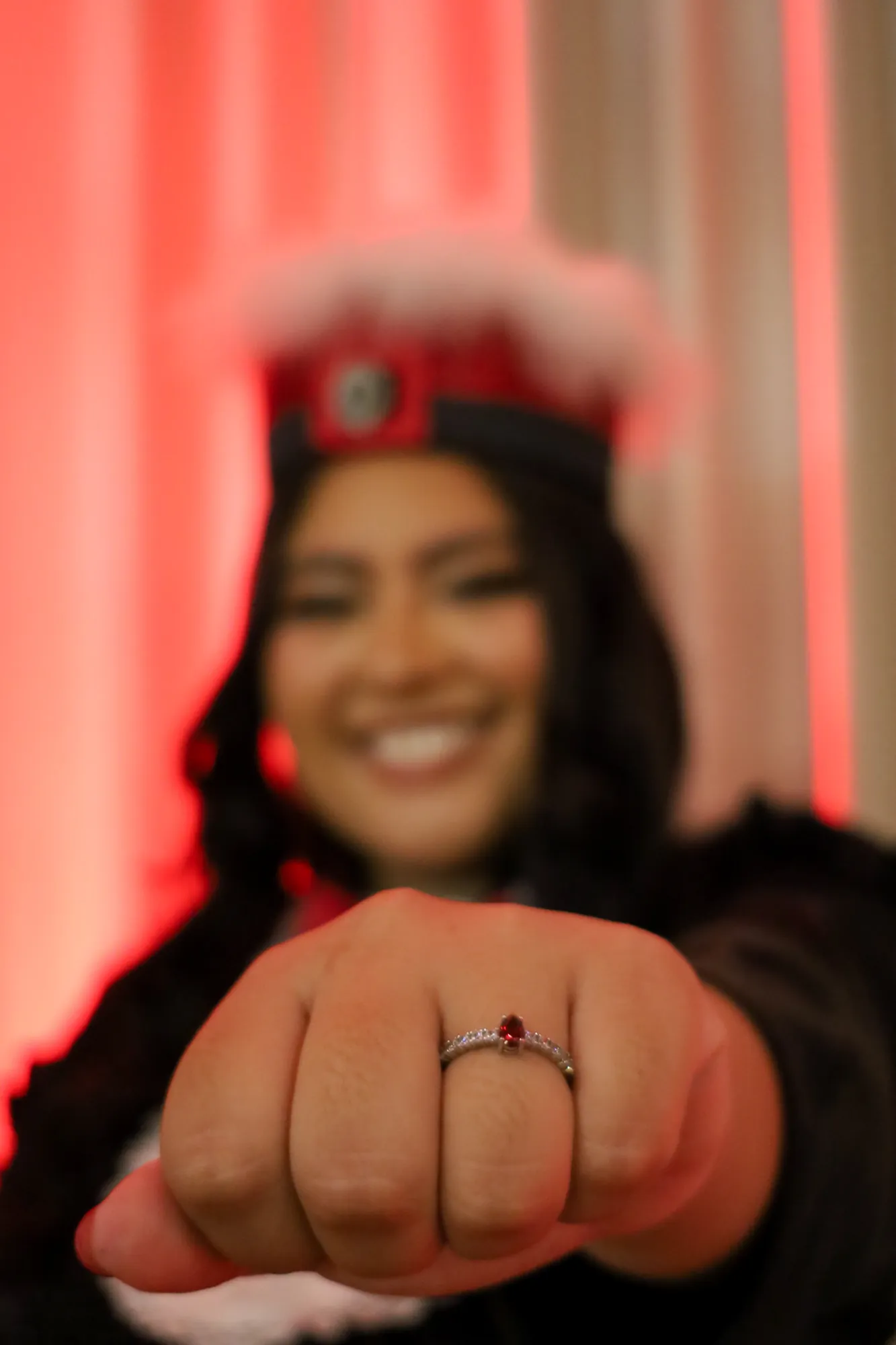 Anel de formatura em primeiro plano, com a formanda sorrindo ao fundo