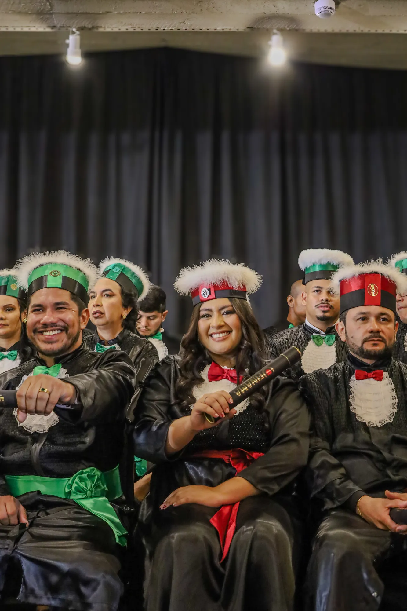 Formandos sorrindo em fileira, de beca e capelo, durante a colação