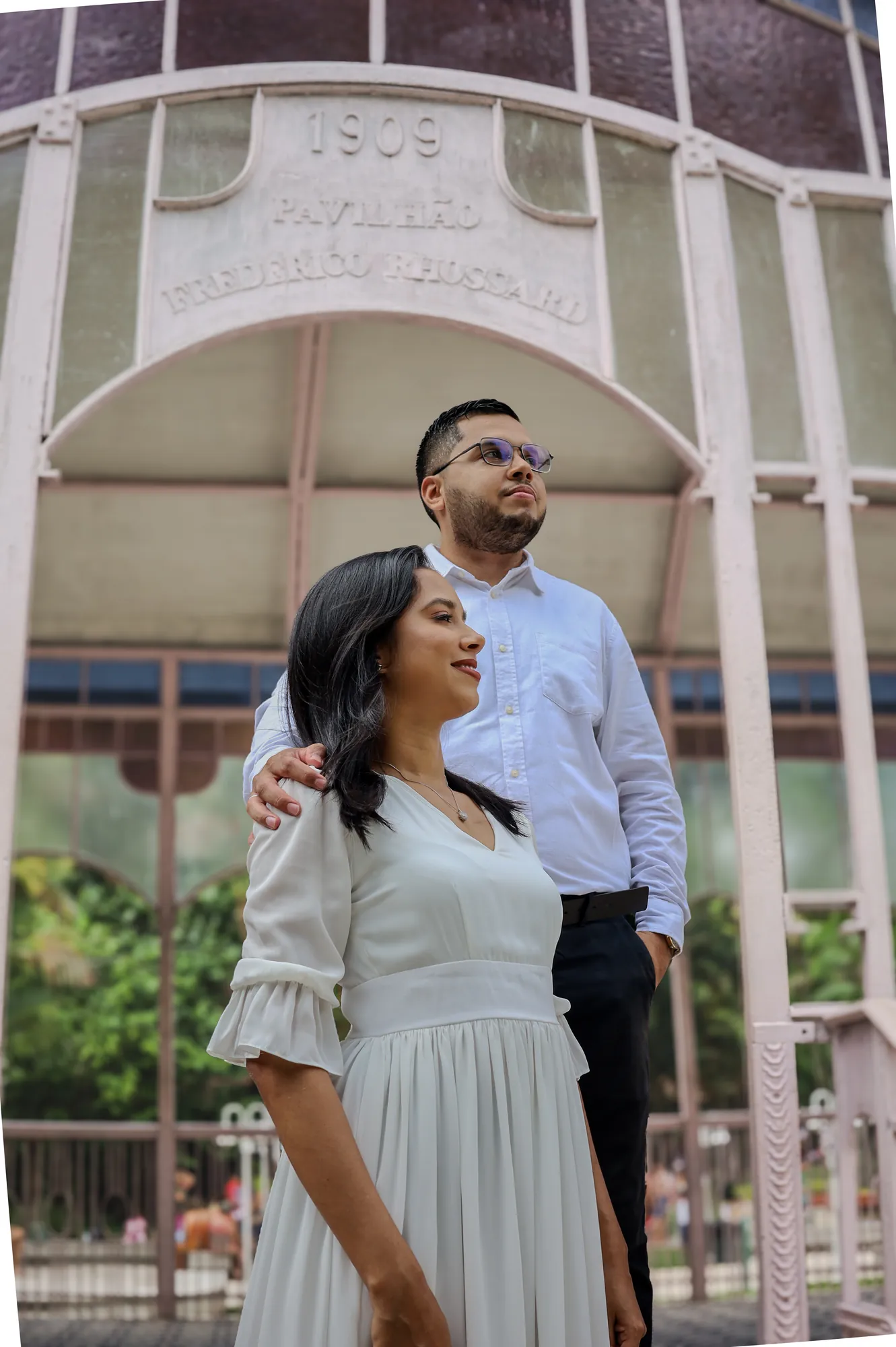 Casal sorrindo sob o arco de um pavilhão histórico