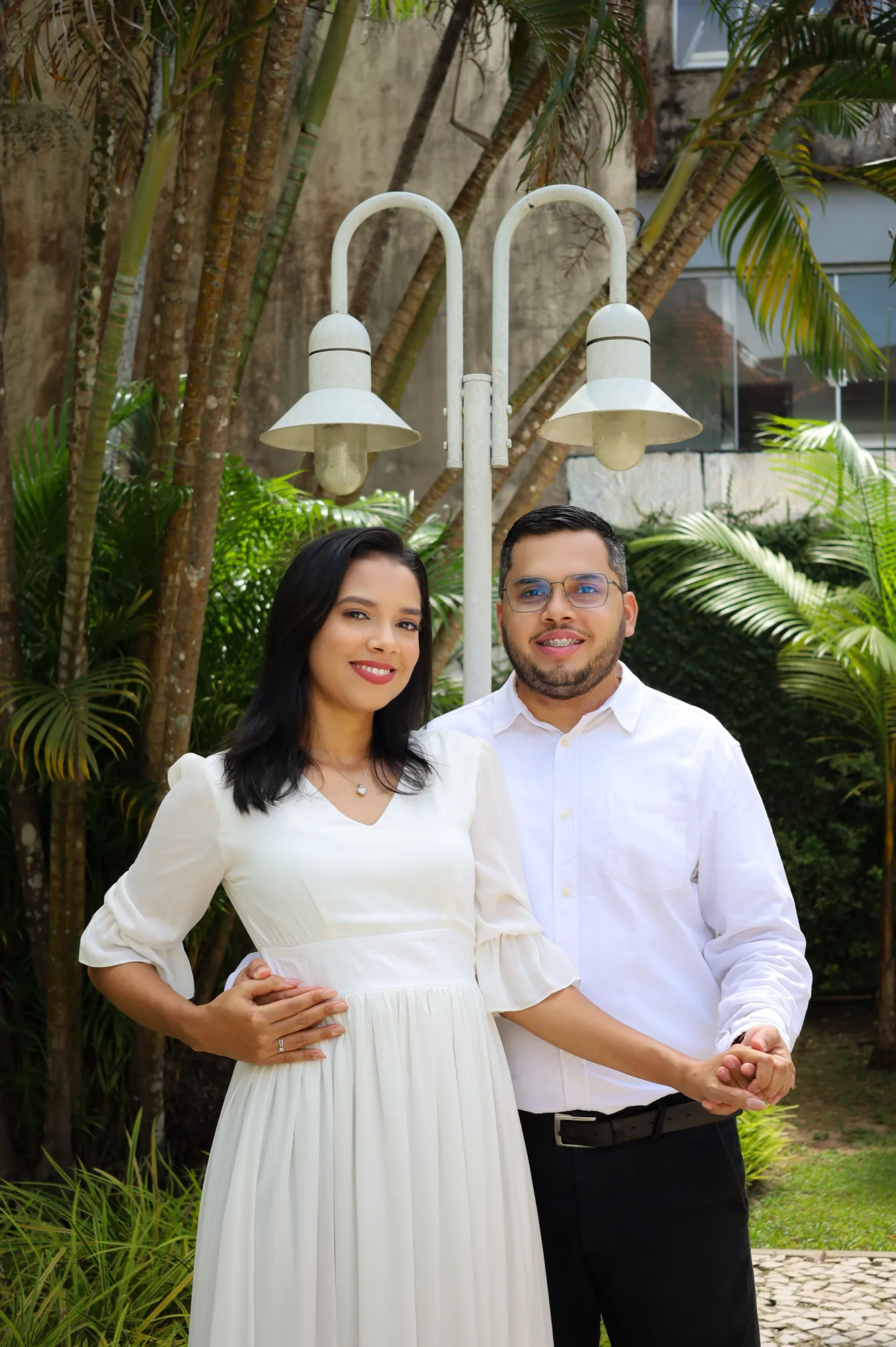 Casal abraçado em jardim com postes de luz e bambus