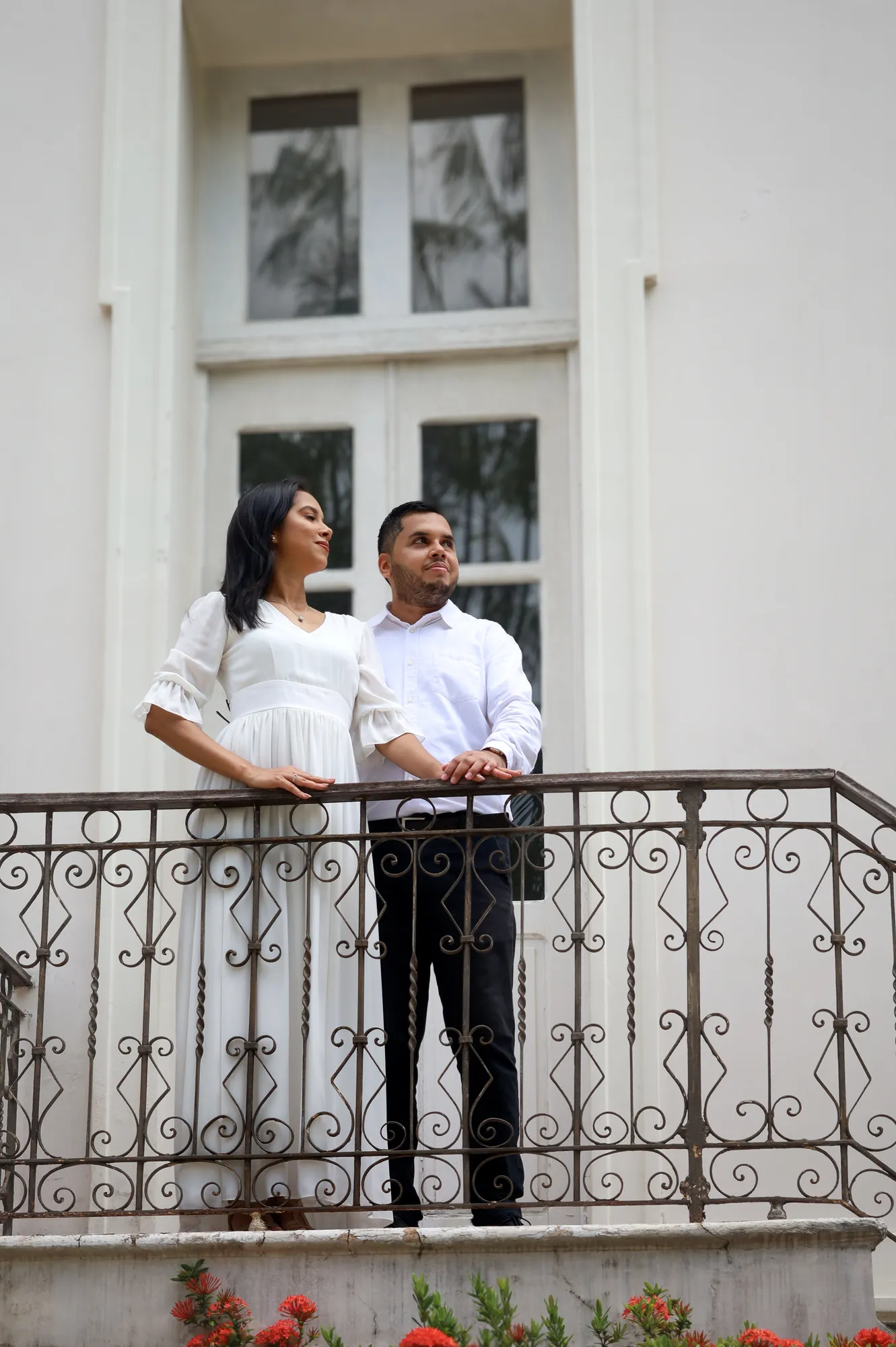 Casal abraçado na sacada de ferro de um casarão branco