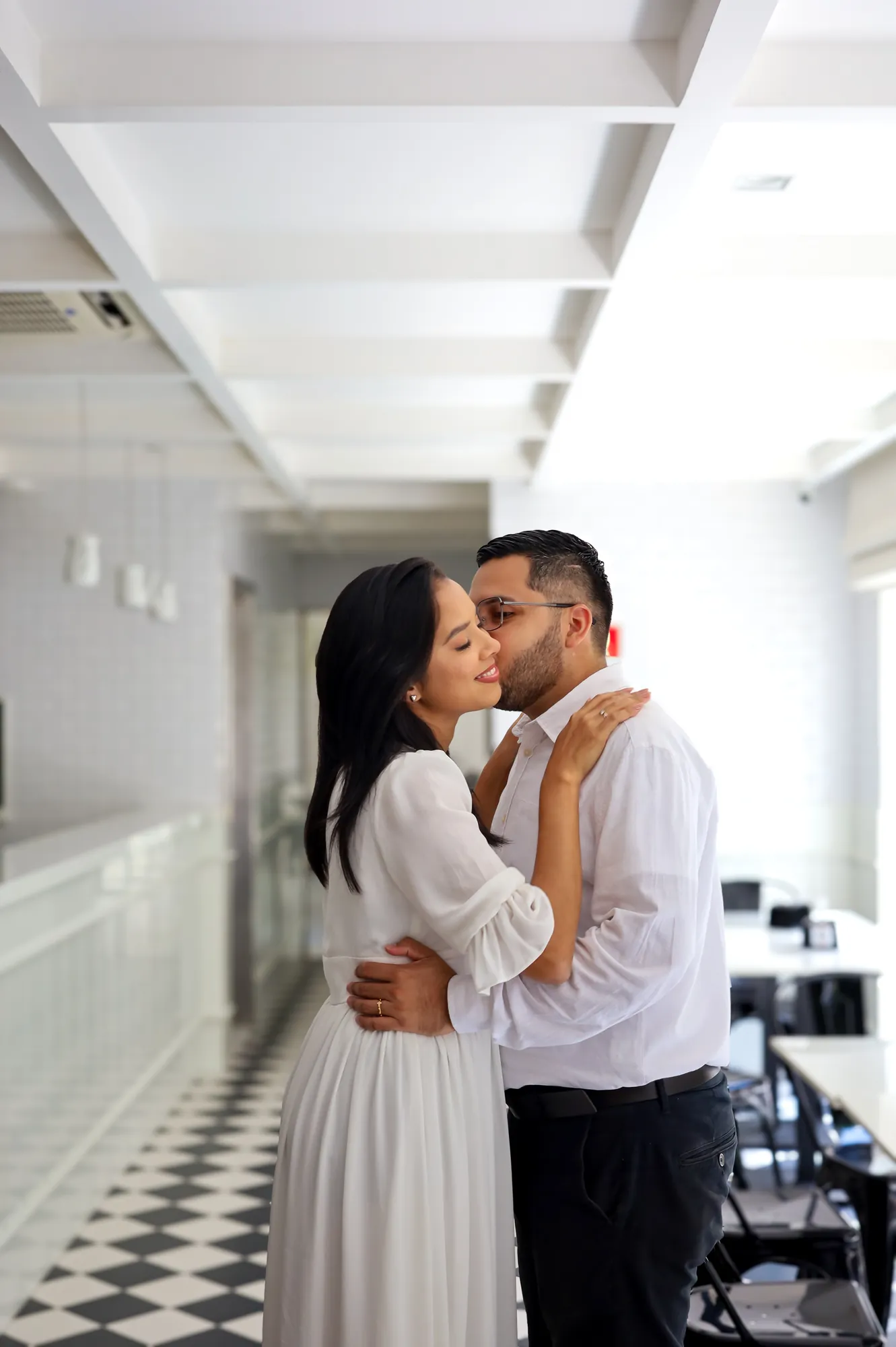 Beijo do casal em corredor de piso xadrez, em luz suave