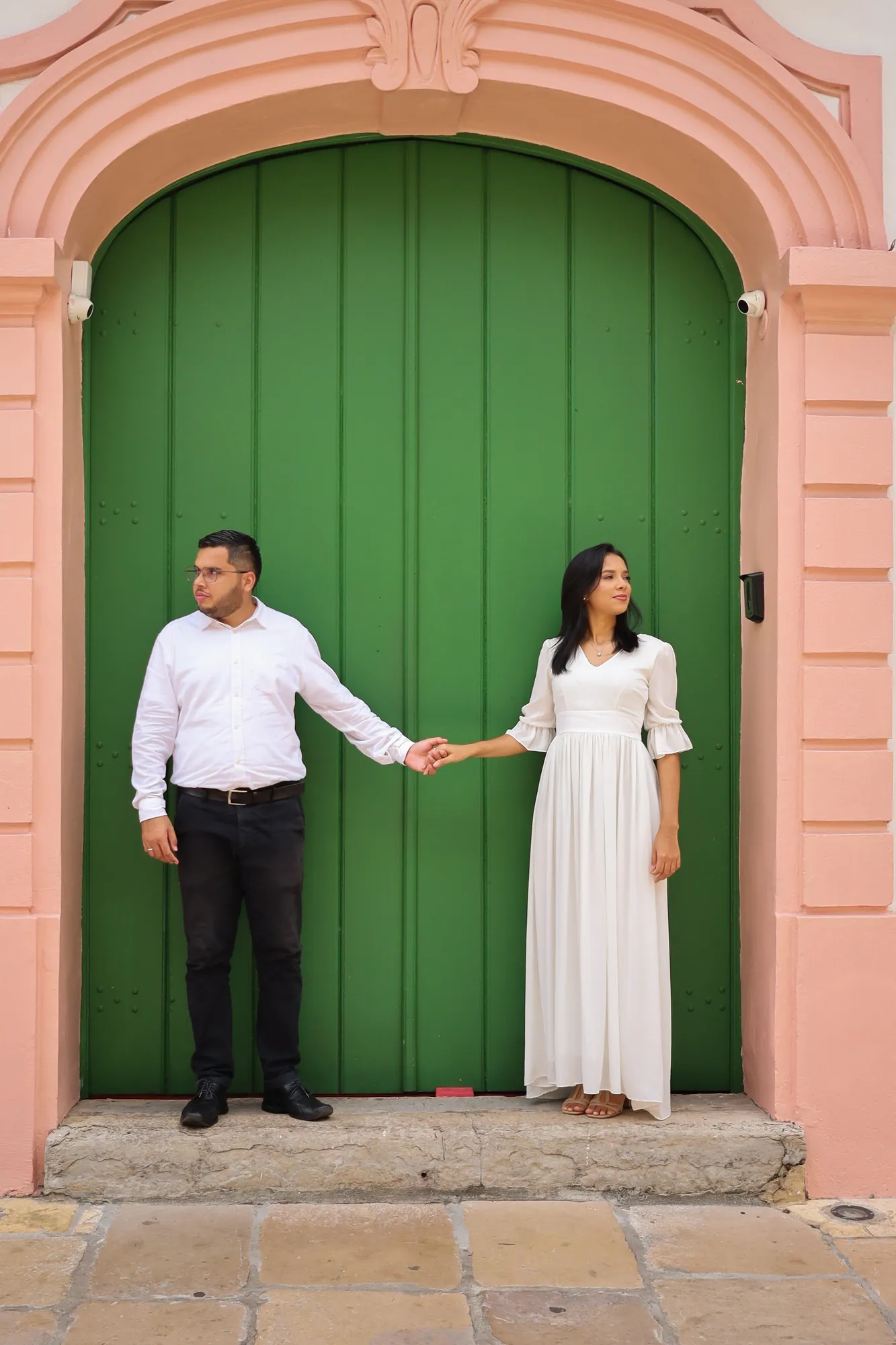 Casal de mãos dadas diante de uma grande porta verde com moldura rosa