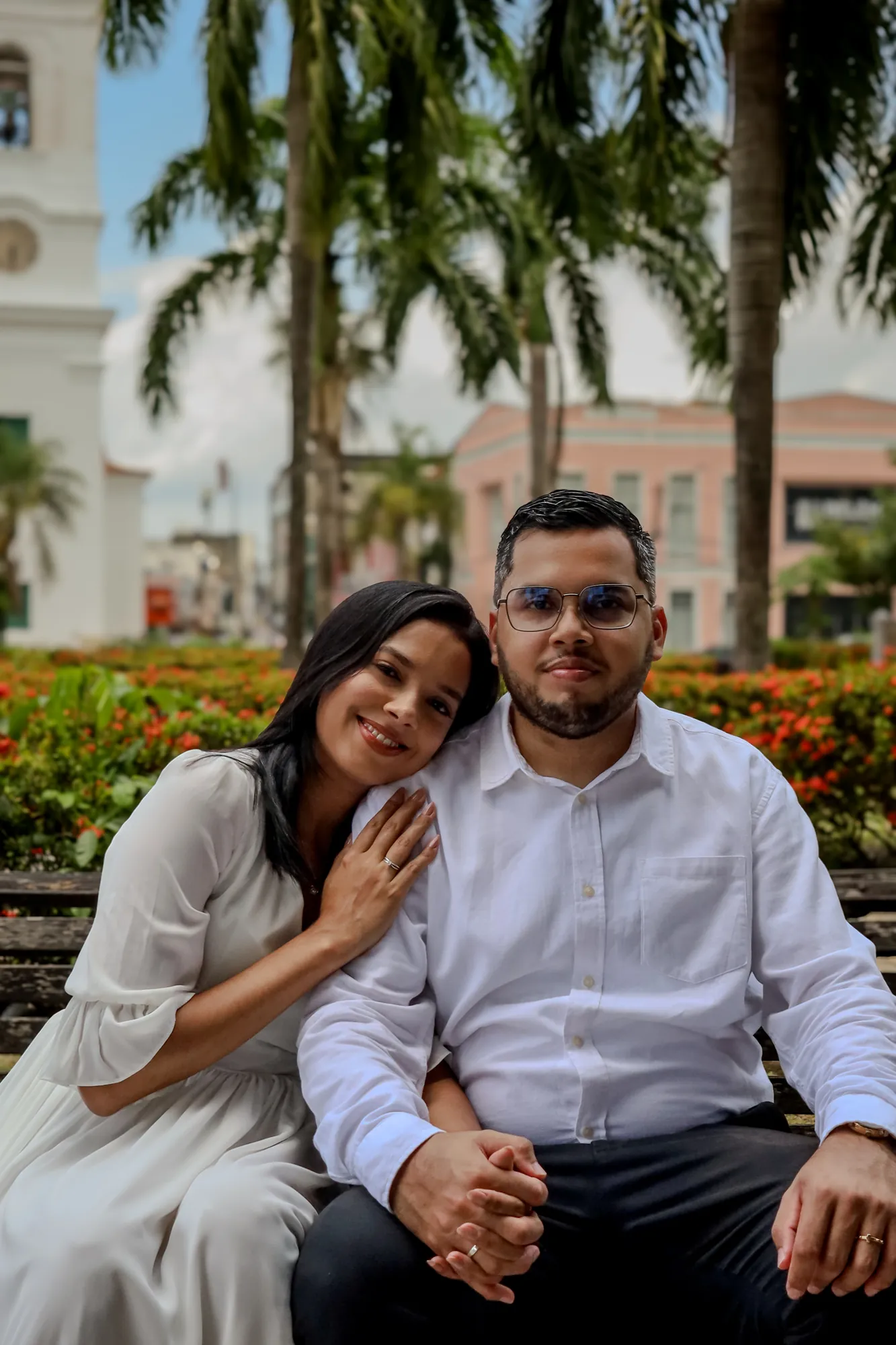 Casal sentado lado a lado, sorrindo, em praça arborizada de Belém